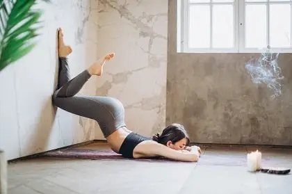 Posture de yoga jambes au mur avec flexion avant, visage au sol pour relaxation et respiration.