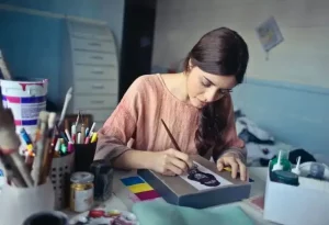 Jeune femme brune , concentrée sur son carnet de croquis, apprenant à dessiner des formes géométriques au crayon dans une lumière naturelle et chaleureuse.