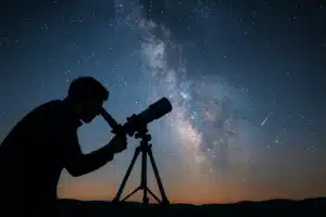 "Un homme observe les étoiles avec un télescope sous un ciel étoilé, parfait pour illustrer les meilleurs livres sur l’espace et l’astronomie"